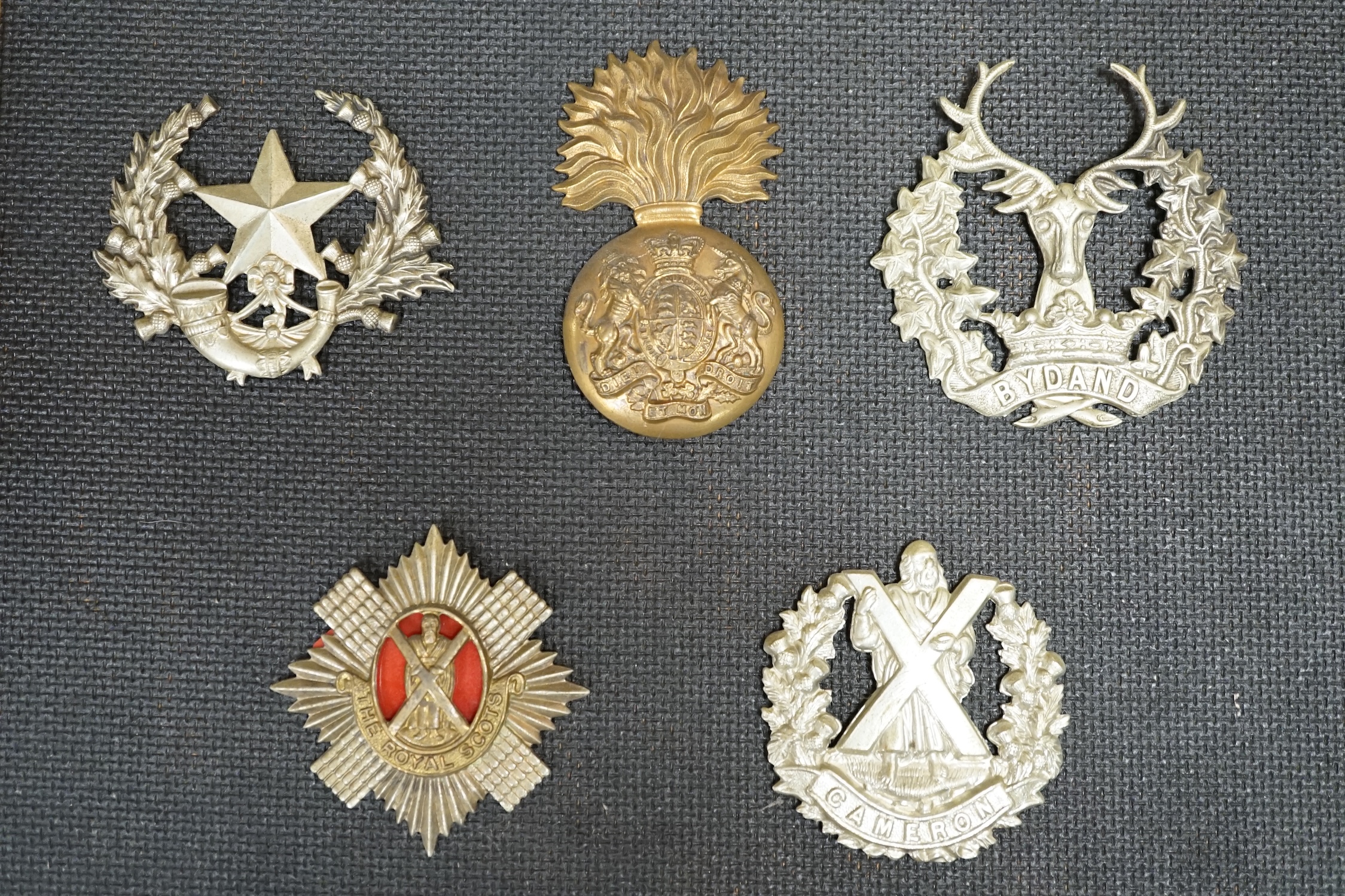 Ten military cap and Glengarry badges mounted on a board including; The King’s Own Scottish Borderers, the Argyle and Sutherland Regiment, the Royal Scots, the Gordon Highlanders, The Queen’s Own Cameron Highlanders, etc